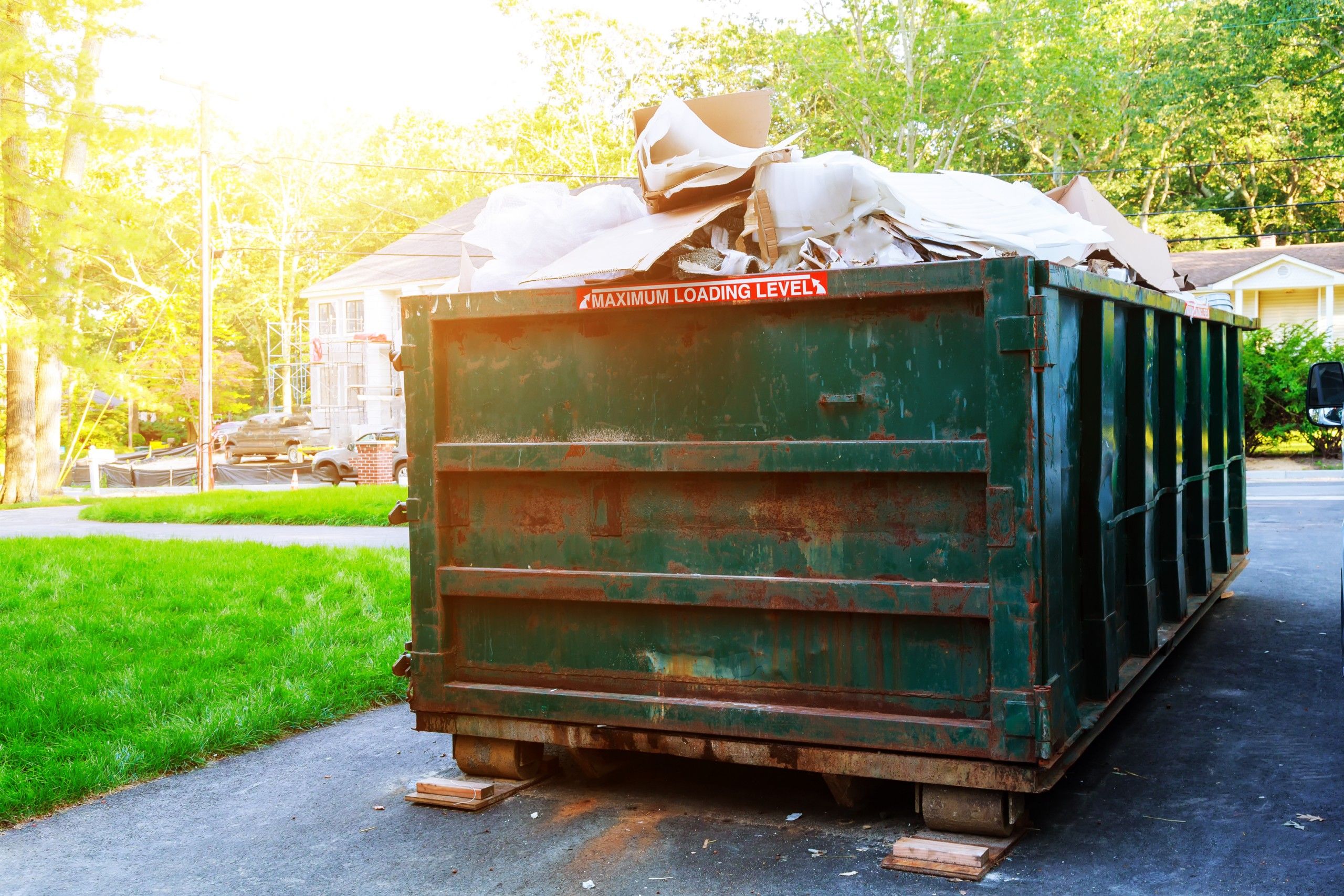 Green roll-off dumpster loaded with debris in a residential driveway